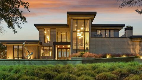 Contemporary two-storey home with glass walls and warm interior lights at dusk
